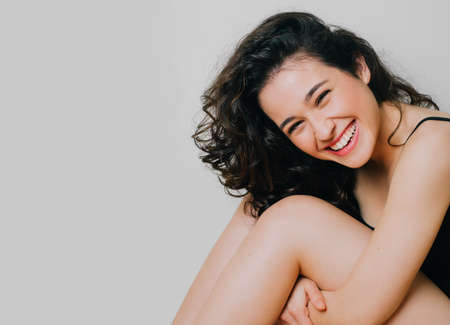 Beautiful brunette young woman with natural wavy hair and clean fresh skin laughing. Beauty and body care concept. Isolated on whiteの写真素材