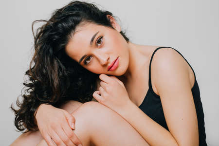 Beautiful brunette young woman with natural wavy hair and clean fresh skin wearing a black top. Beauty and body care concept. Isolated on whiteの写真素材