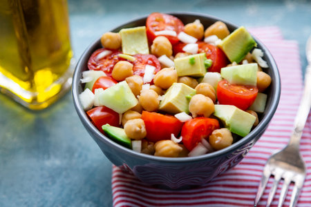 Healthy and delicious chickpea salad with  cherry tomato, avocado, cucumber and onion in a bowl un a rough blue backgroundの写真素材
