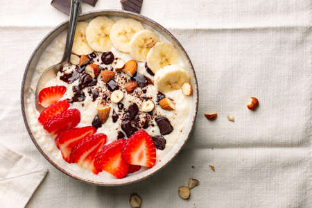 Millet porridge with strawberry, banana, dark chocolate pieces, hazelnut and almond in a ceramic bowl on a white napkinの写真素材