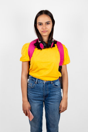 Portrait of a somewhat ungainly and serious teen girl with backpack and headphones holding a mobile phoneの写真素材