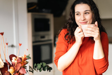 Young happy woman enjoying a hot drink in the kitchen with a dreamy lookの写真素材