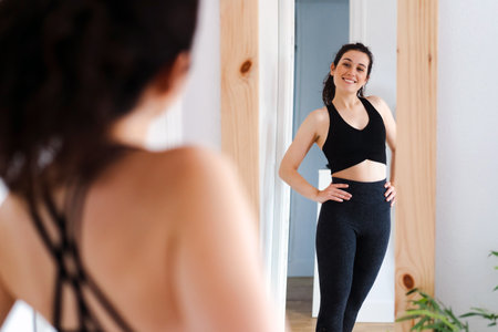 Young happy beautiful woman looking in the mirror satisfied with the results of her training
