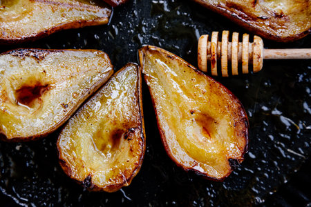 Baked pears with honey, Modena vinegard and cinnamon, and honey dipper in a baking trayの写真素材