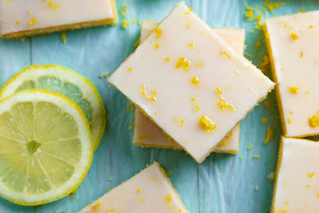 Fudgy lemon brownies with lemon glaze and zest on baking paper on an aquamarine backgroundの写真素材