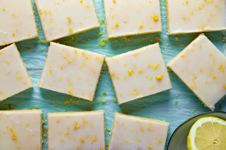 Fudgy lemon brownies with lemon glaze and zest on baking paper on an aquamarine backgroundの写真素材