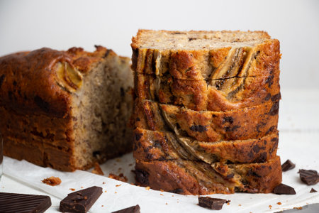 Sliced moist banana bread with oats and dark chocolate chunks on a white wooden table