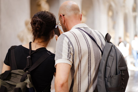 Rear view of father and daughter with backpacks sharing the audio guide in a museum. Cultural family...