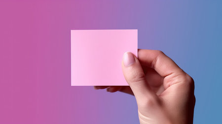 Female hand holding a pink sticky note on a blue background with copy spaceの素材