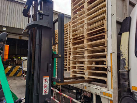 Worker driving forklift truck to unload wooden pallets stack from truck to the cargo warehouse to...