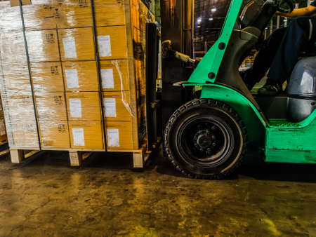 Worker driving forklift loading and unloading shipment carton boxes and goods on wooden pallet from container truck to warehouse cargo storage in logistics and transportation industrialの写真素材