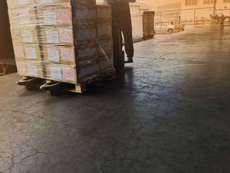 Worker driving forklift loading and unloading shipment carton boxes and goods on wooden pallet from container truck to warehouse cargo storage in logistics and transportation industrialの写真素材