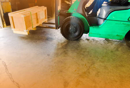 Worker driving forklift loading and unloading shipment carton boxes and goods on wooden pallet from...