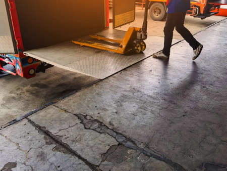Worker driving forklift loading and unloading shipment carton boxes and goods on wooden pallet from container truck to warehouse cargo storage in logistics and transportation industrialの写真素材