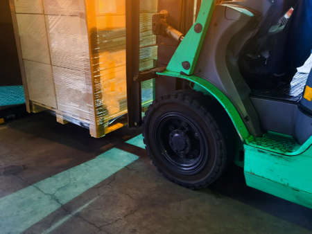 Worker driving forklift loading and unloading shipment carton boxes and goods on wooden pallet from...