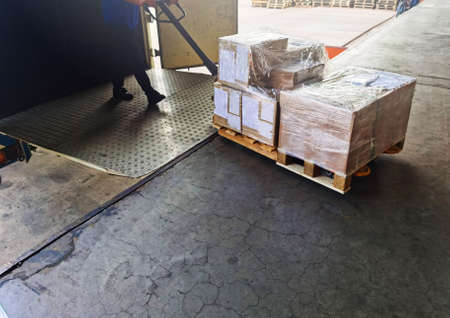 Worker driving forklift loading shipment carton boxes goods on wooden pallet at loading dock from...