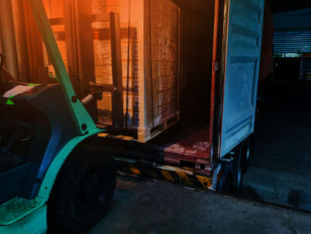 Worker driving forklift loading shipment carton boxes goods on wooden pallet at loading dock from...