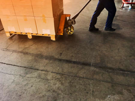 Worker driving forklift loading shipment carton boxes goods on wooden pallet at loading dock from...