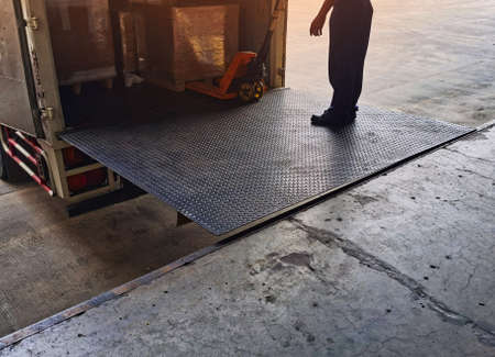 Worker driving forklift loading shipment carton boxes goods on wooden pallet at loading dock from...