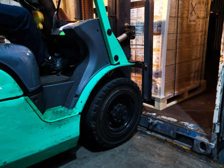 Worker driving forklift loading shipment carton boxes goods on wooden pallet at loading dock from...