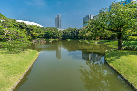 Tokyo, Bunkyo Ward - August 04, 2018 : Daisensui pond at Koishikawa Korakuen Garden, skycrapers and Tokyo Dome Stadium in the backのeditorial素材