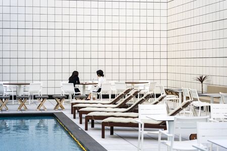 Two Ladies Are Sitting And Talking Next To Open Air Swimming Pool.の写真素材
