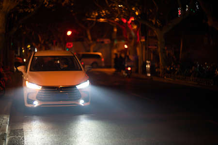 SHANGHAI, CHINA - NOVEMBER 28, 2018. Retro film photo with blurred background. Car's front lights illuminate on a polluted day at night time. Lamps of white vehicle light up air pollution in the Chinese city.のeditorial素材