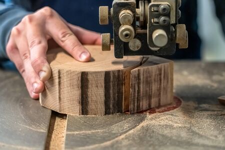 Carpenter is cutting the wooden piece by equipment on stand. The man's hand is making a round detail from the log. Joiner is using Electric fret saw to make a bowl at the workshop.の写真素材