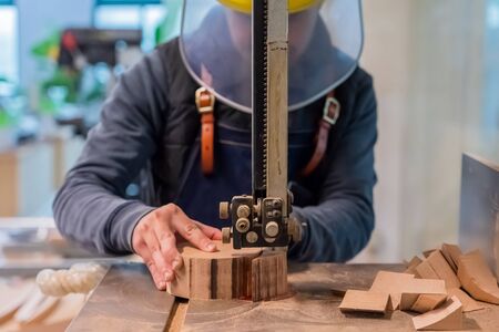 Carpenter is cutting the wooden piece by equipment on stand. The man's hand is making a round detail...