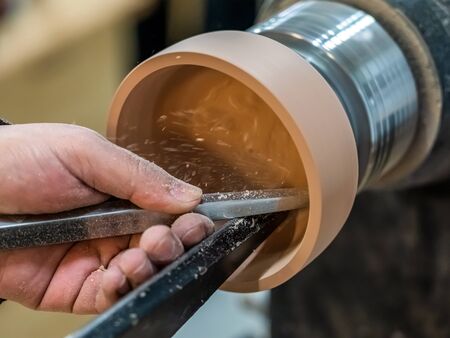 Carpenter man is shaving the wooden bowl. Spinning wood wheel. Carving inside forming a round detail. Joiner is using metal tool to make the handmade pot at workshop. Hand is polishing surface.の写真素材