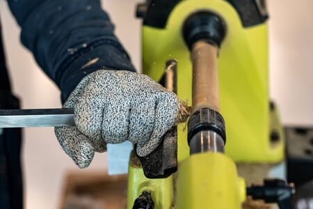Carpenter man is carving the wooden stick. Spinning wood wheel machine. Trimming forming a round detail. Joiner is using metal tool to make the handmade decoration at workshop.の写真素材