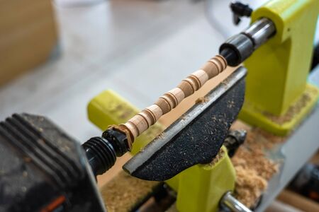 The nicely decorated detail set in spinning machine at workshop. Joiner is making wooden fretwork stick. Carpenter finished woodwork model and sawdust on blurred background.の写真素材