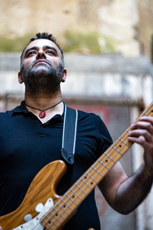Handsome Male Person is Playing on Bass Guitar on Street. Caucasian Young Person Performing at Outdoor Event.の写真素材