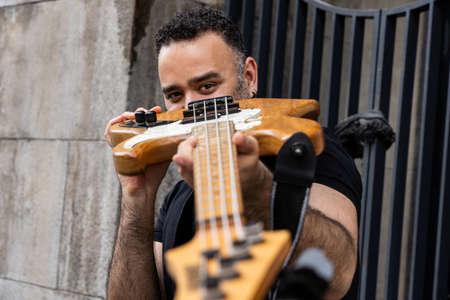 Handsome Male Person is Looking Through his Bass Guitar on Street. Playful Caucasian Young Person at Outdoor Event.の写真素材