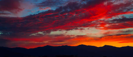 The last rays of the sun from behind the mountains illuminated clouds in unreal beautiful colors.の写真素材