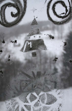 Winter Christmas drawing on transparent glass, behind which is visible winter landscape Ukrainian Carpathian Mountainsの写真素材