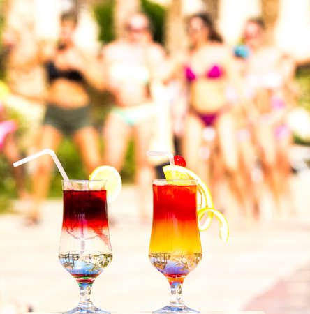 Beautiful multi-colored cocktails on swimming pool background, girls and palm treesの写真素材