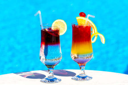 Beautiful multi-colored cocktails on swimming pool background, girls and palm treesの写真素材
