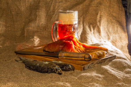 Smoked fish, dried fish, wooden board, knife, beer, burlap.の写真素材