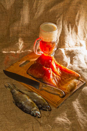 Smoked fish, dried fish, wooden board, knife, beer, burlap.の写真素材
