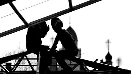Workers builders high-builders build a roof at the height of the domes of the church. Black and white photo. Silhouettes and
Contours. Workers sit on the roof structures in profile faces facing each other.の写真素材