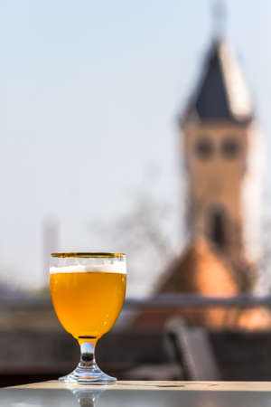 A glass of unfiltered beer looks gorgeous against the background of the old buildings of the beautiful city of Mukacheve, Ukraineの写真素材