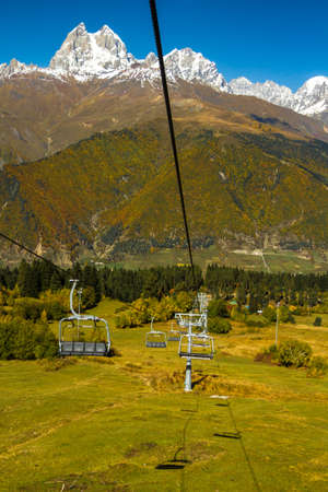 Humped peak of Mount Ushba, Georgia. Down in the early autumn, warmth and trees in the autumn crimson foliage. The peak and the mountain chain are in the snow.の写真素材