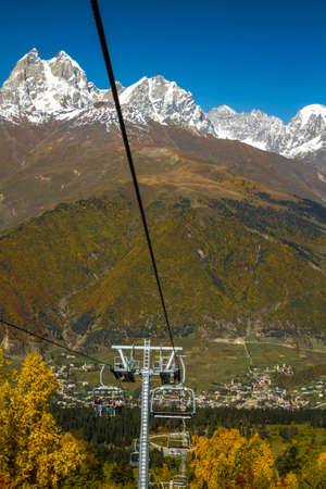 Humped peak of Mount Ushba, Georgia. Down in the early autumn, warmth and trees in the autumn crimson foliage. The peak and the mountain chain are in the snow.のeditorial素材