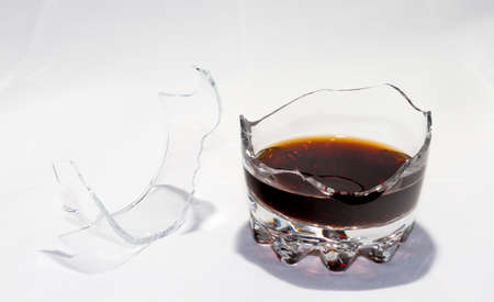 A broken whiskey glass with the remains of whiskey stands on a white background. There are splinters nearby.の写真素材