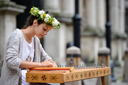 RIGA, LATVIA - JULY 27, 2016: Unknown girl in traditional costume on the street plays a harp.