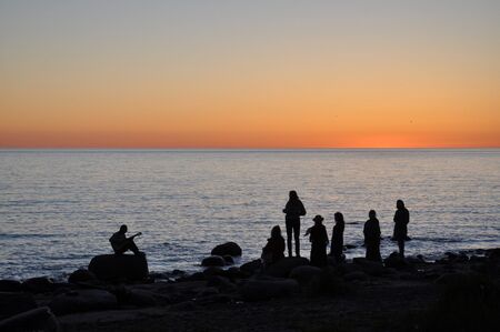 People silhouettes on the seashore at sunset.の写真素材