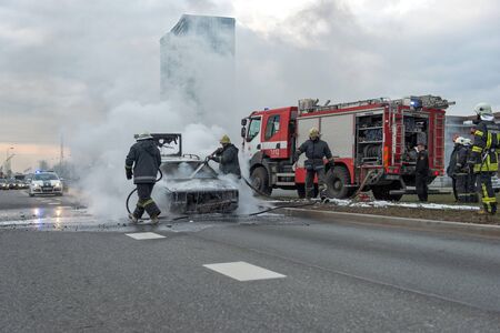 RIGA, LATVIA - APRIL 11, 2014: A few minutes in the street burnt car. Traffic is stopped. Firefighters eliminate fire.のeditorial素材