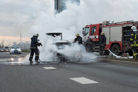 RIGA, LATVIA - APRIL 11, 2014: A few minutes in the street burnt car. Traffic is stopped. Firefighters eliminate fire.のeditorial素材