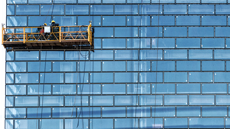 Workers, standing in the ropes installation basket, wash skyscraper windows from the outside.の写真素材